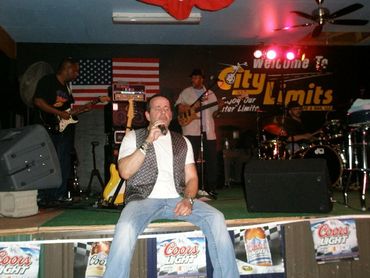 Band performing live on stage with singer in front and American flag backdrop.