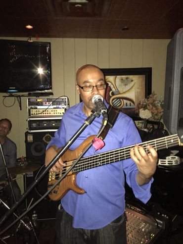 Man in a blue shirt playing bass guitar and singing into a microphone.