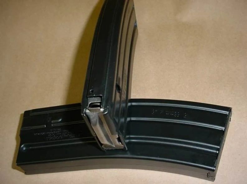 Two black metal firearm magazines on a beige surface.