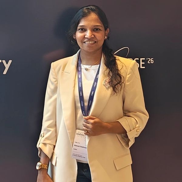 Smiling woman in a beige blazer with a conference badge and lanyard.