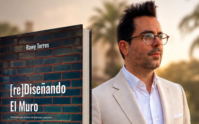 Author Rawy Torres stands beside his book '[re]Diseñando El Muro' about healthy relationships.
