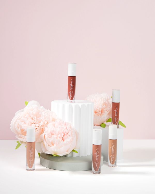Elegant lip gloss tubes with soft pink flowers and pastel background.