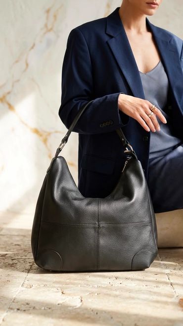 Woman in navy blazer holding a large black leather handbag.