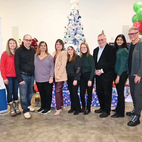 Group of nine people posing in front of a decorated white Christmas tree indoors.