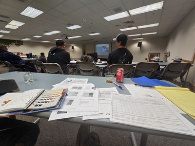 Classroom scene with students facing a presentation, study materials on the desk.