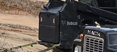 Black construction trucks parked on a sandy lot with autumn trees in the background.