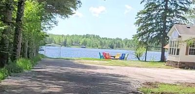 A lakeside scene with colorful chairs and a cabin near a dirt road.
