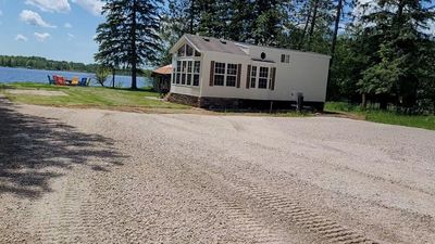 Small white house near a lake with colorful chairs by the water.