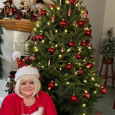Woman in Santa hat by decorated Christmas tree.
