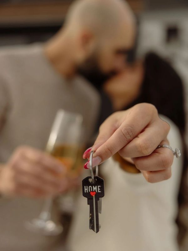 Couple holding a key with 'HOME' written on it, celebrating with a drink.