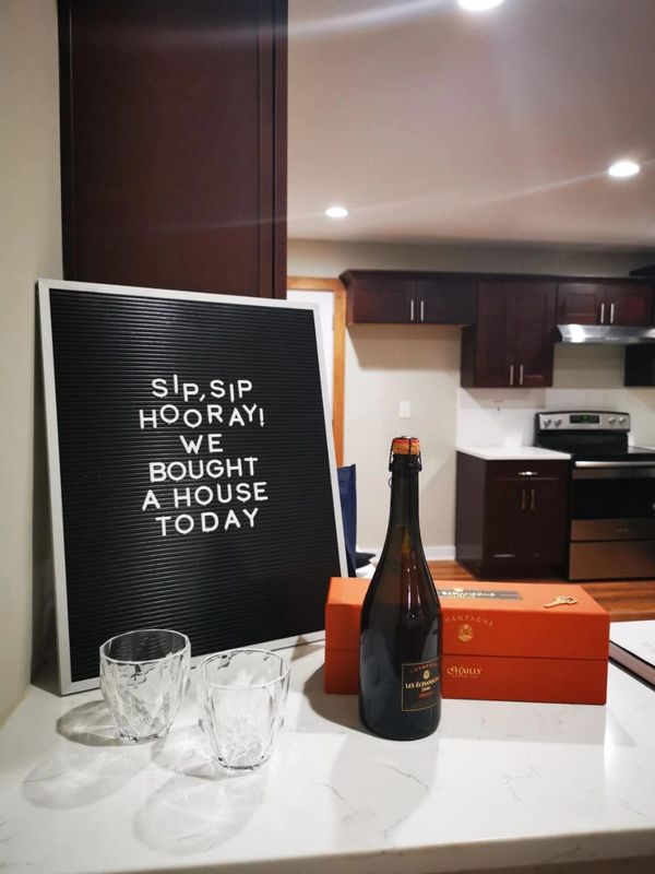 Celebration setup with champagne and a sign announcing a new house purchase.