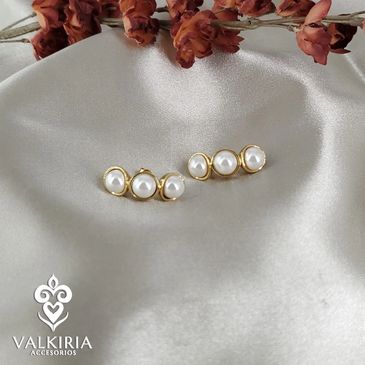 Elegant pearl and gold stud earrings on silky fabric with dried flowers.