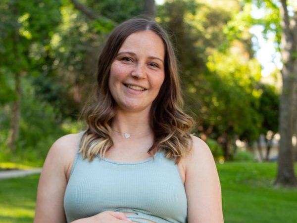 Smiling woman outdoors wearing a light blue tank top with nature background.
