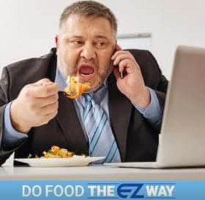 Man eating while talking on phone at his desk with laptop.