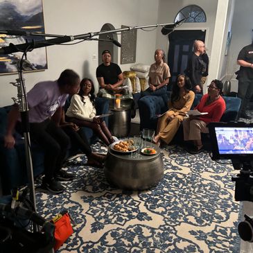 Group of people filming a casual discussion scene in a cozy living room.