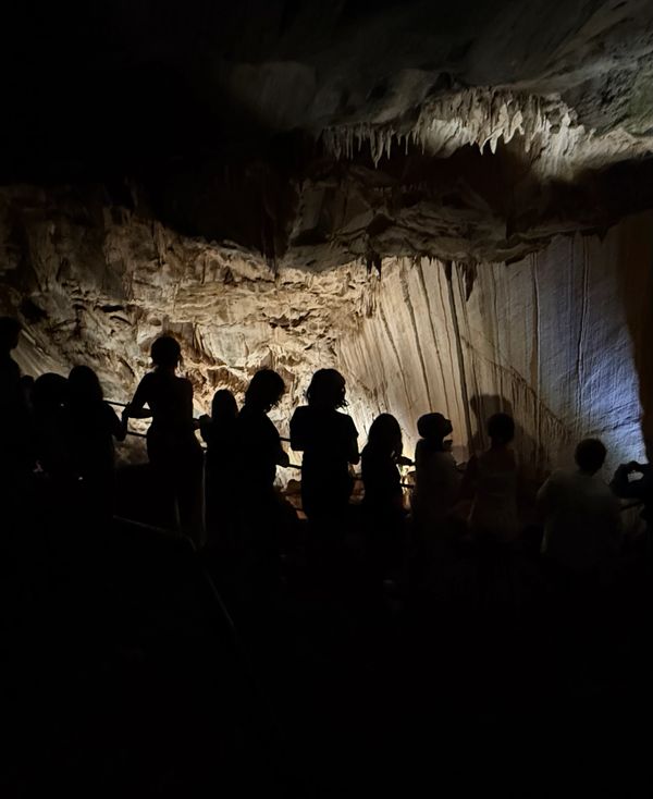 Silhouetted group exploring a dimly lit cave with stalactites on the ceiling.