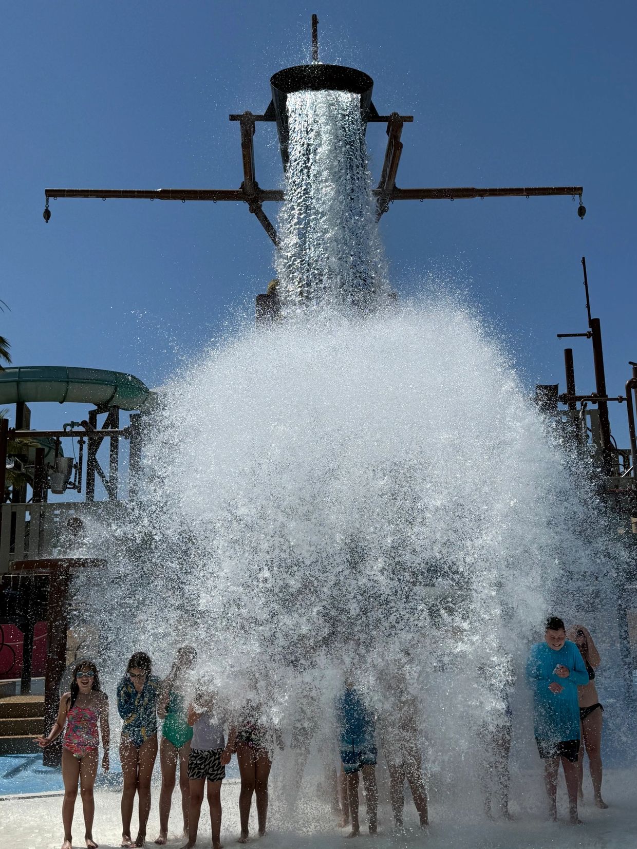 Group of people getting splashed by a large bucket of water at a water park.
