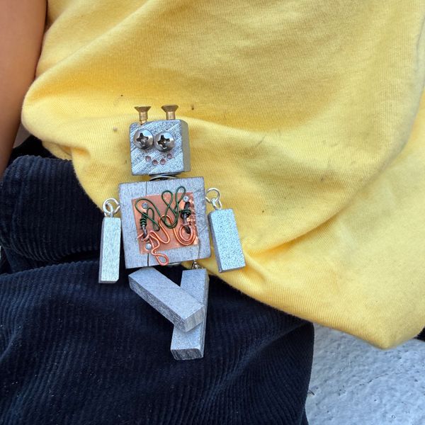 Small handmade robot figure with screws and wires on black and yellow fabric.