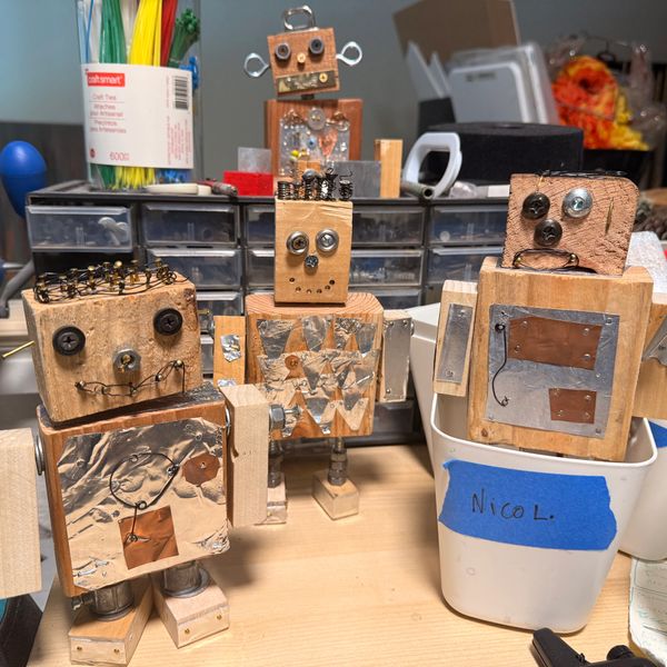 Four handmade wooden robots with metal details on a cluttered desk.