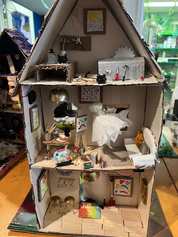 Detailed three-story miniature dollhouse made from cardboard with artistic and household elements.