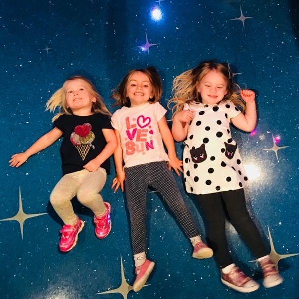 Three joyful girls lying on a starry blue floor, smiling and having fun.