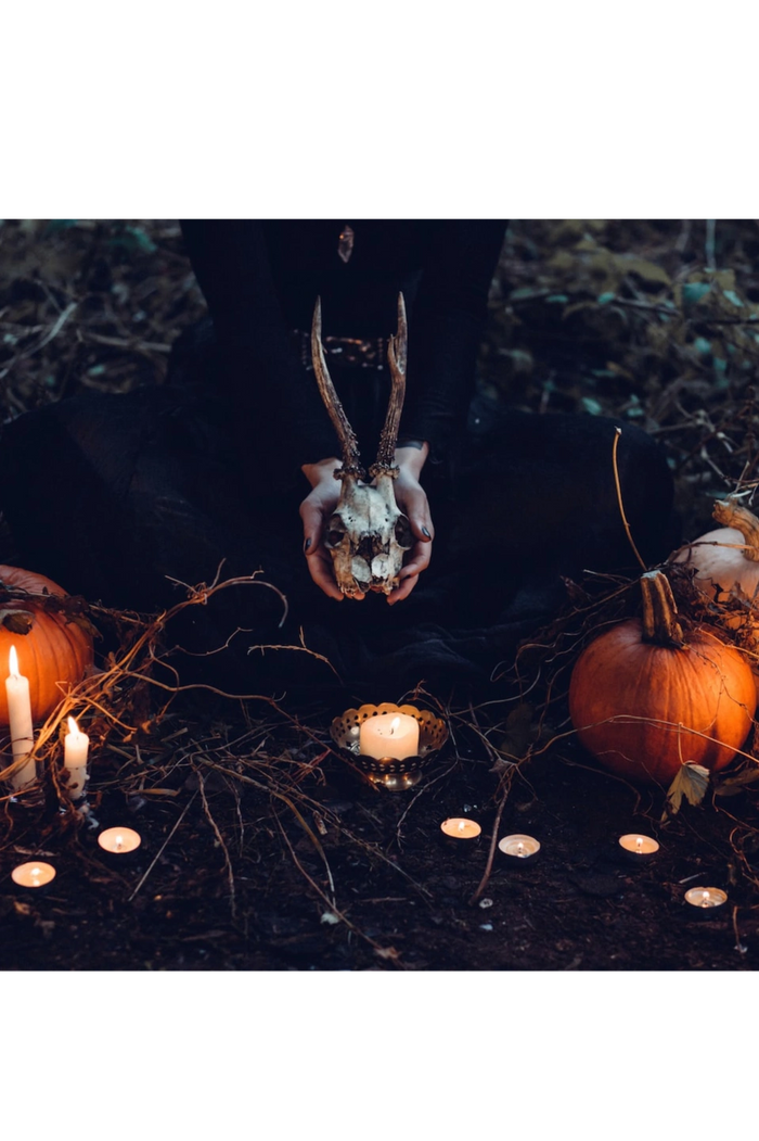 candles, pumpkins and hands holding a deer skull