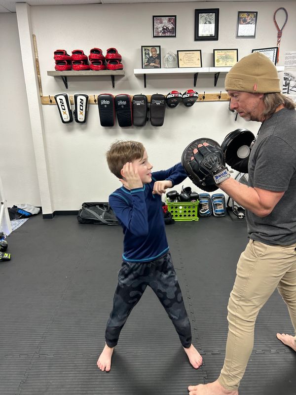A young boy practicing boxing with an adult trainer in a gym.