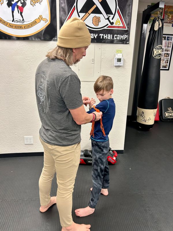 Man teaches young boy Muay Thai wrist wrapping in a gym.