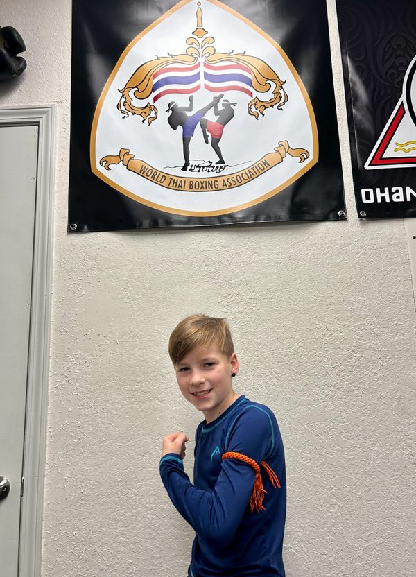 A young boy posing confidently in front of a World Thai Boxing Association banner.