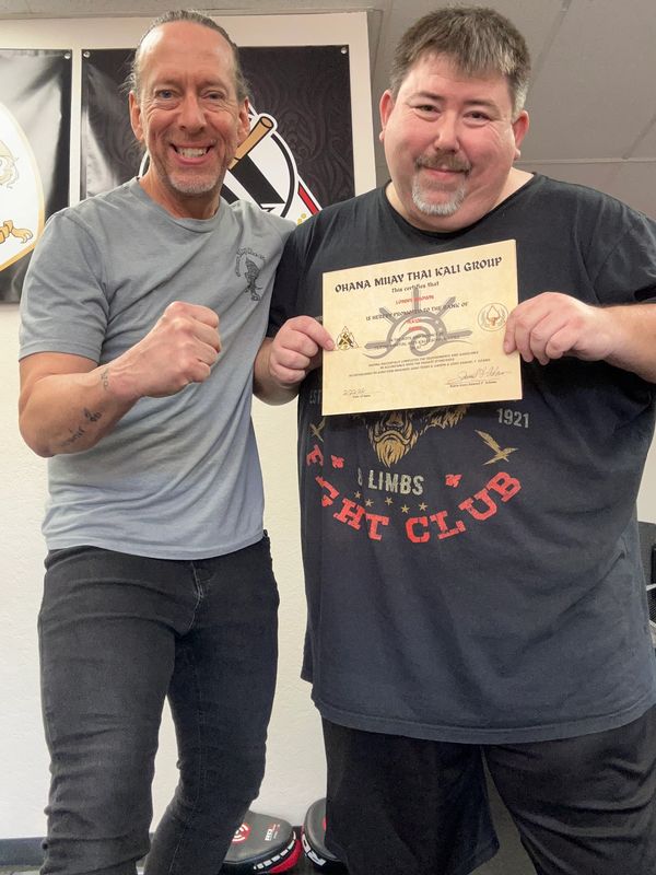 Two men smiling, one holding a martial arts certificate.