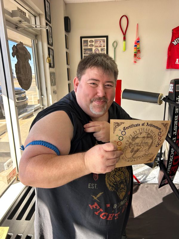 A man proudly shows a certificate of achievement in a gym setting.
