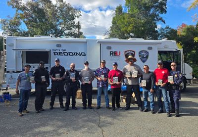 Group of emergency responders and officials posing with plaques in front of a City of Redding vehicle.