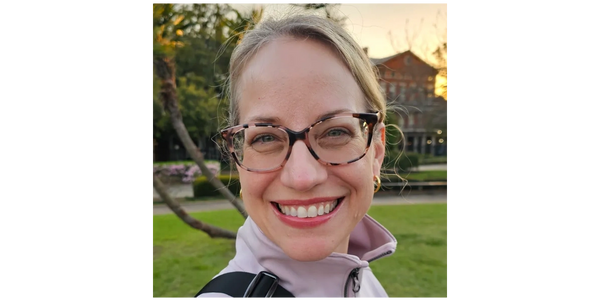 A smiling woman with glasses outdoors in a park during sunset.