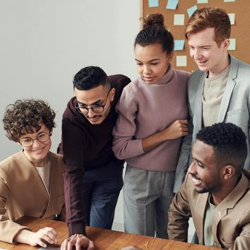A diverse group collaborating and smiling around a laptop in an office setting.