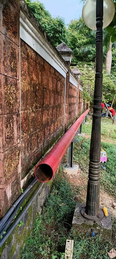 Red pipe alongside an old brick wall with a tall lamp post.