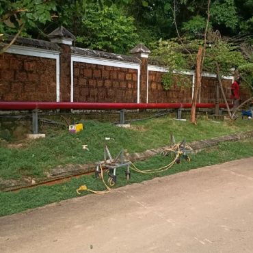 Red pipeline along a stone wall with construction tools nearby.