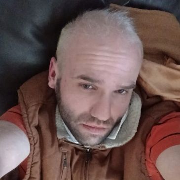Man with light hair and beard wearing brown jacket.