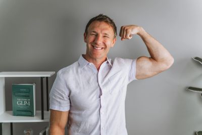 Smiling man flexing bicep in casual shirt.