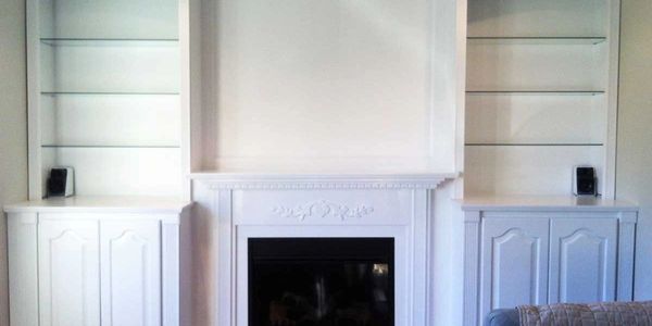 White built-in shelves and cabinets flanking a decorative fireplace.