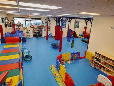 A view from the top of our zipline over the the gym. There is a blue mat floor, zipline, swings, sma