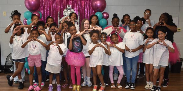Group of girls and women making heart signs in front of balloon decoration.