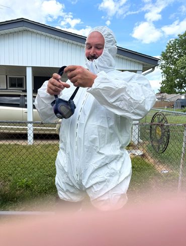 Man in white hazmat suit holding a respirator mask outdoors.