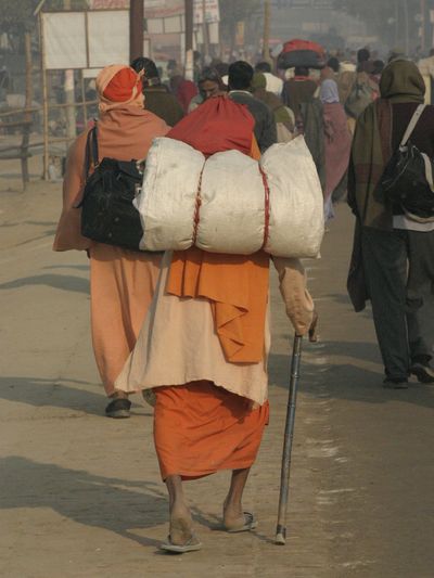 Person walking with heavy load and cane on busy street.