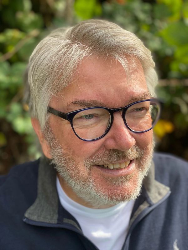 Smiling elderly man with glasses outdoors.