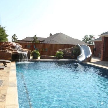 Backyard swimming pool with slide and waterfall feature.