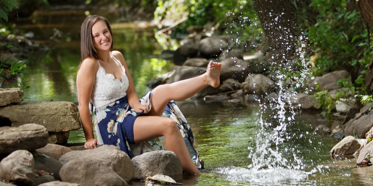 Senior photo of Mackenzie Leeman sitting on a rock and splashing water with her foot.