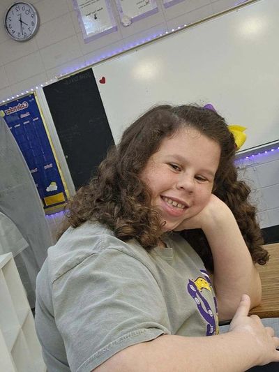 A smiling girl with curly hair sitting in a classroom.