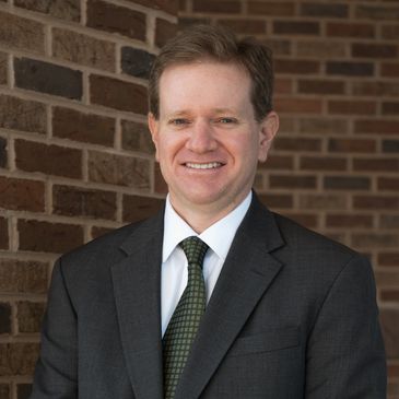 Smiling man in a suit standing against a brick wall.