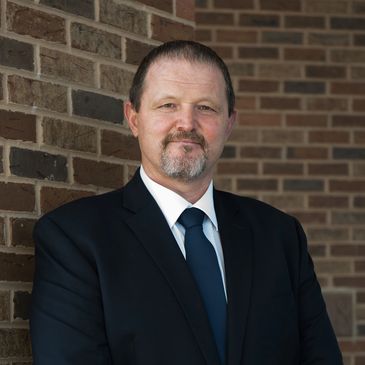Man in a suit standing against a brick wall.
