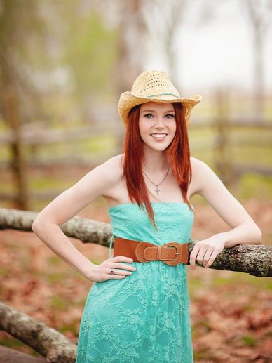 Young woman in a turquoise dress and cowboy hat smiles outdoors.